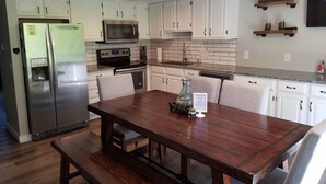 A modern kitchen with white cabinets, stainless steel appliances, and a wooden dining table with chairs. - The Mountains Win Again (Lake Lure)
