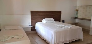 A hotel room with a large bed, a smaller bed, a nightstand, a bedside table, and a wall-mounted shelf with a vase. - Hotel do Porto (Porto Franco)