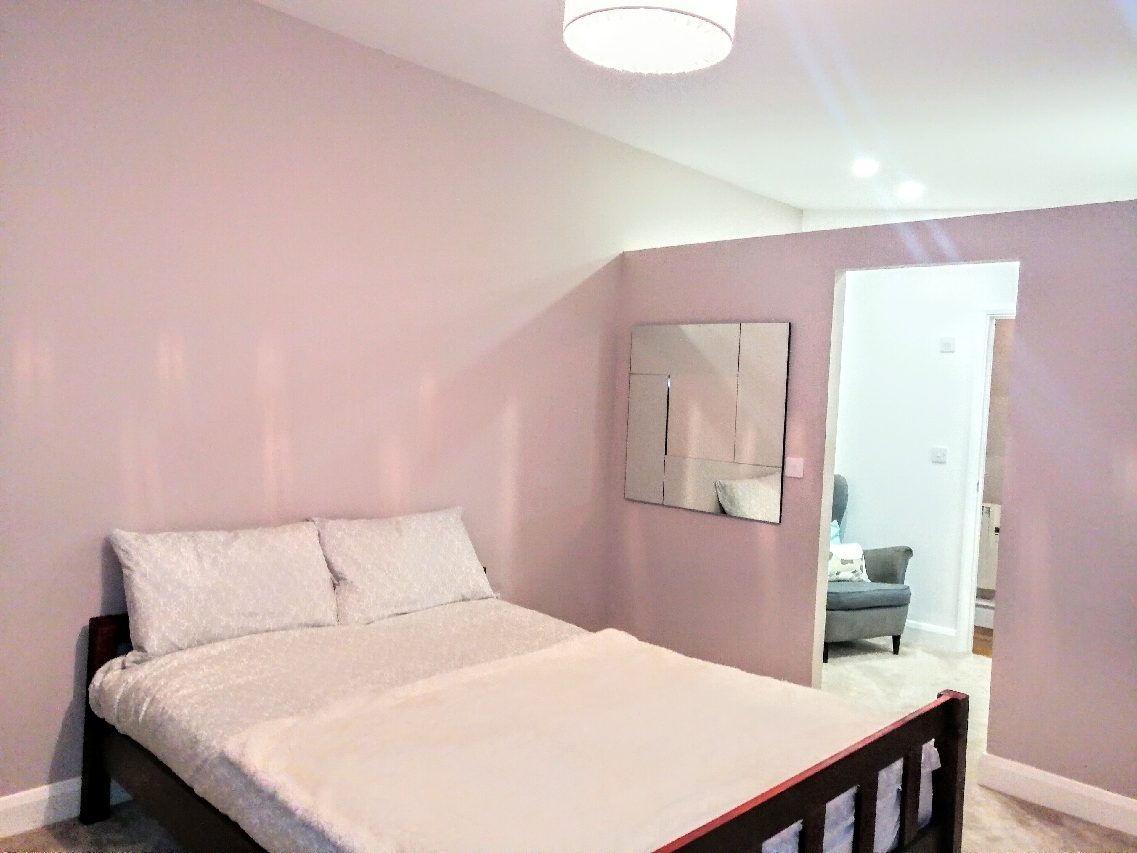 Un dormitorio con una cama, un espejo en la pared y una puerta que da a otra habitación.