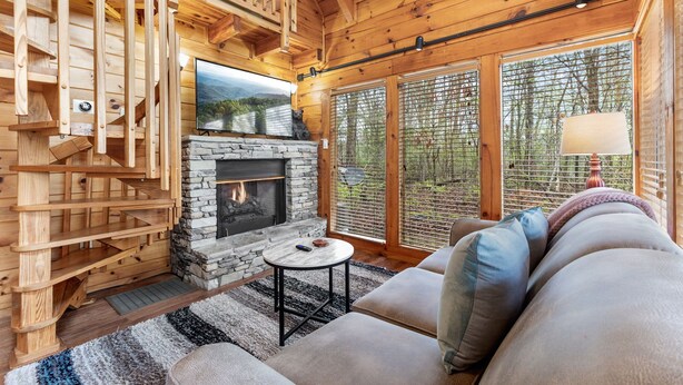 A cozy cabin interior with a stone fireplace, wooden staircase, and a comfortable seating area with a sofa and a small table. - Time to Get Cozy! King Bed I Hot Tub I Foosball Table I Cabin for Couples (Sevierville)