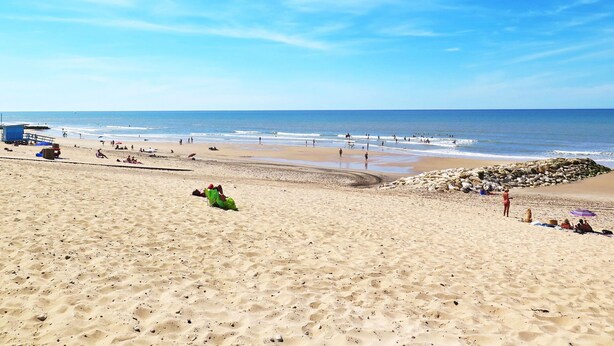 Una playa con una torre de salvavidas, arena y vista al océano.