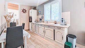 Una cocina compacta con comedor, que incluye una encimera blanca, armarios y un ventanal con cortinas.