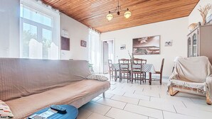 Una sala de estar acogedora con techo de madera, un sofá, una mesa de comedor con sillas y una butaca tapizada.