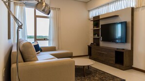 Ett modernt vardagsrum med en soffa, ett soffbord, en tv på ett träställ och ett fönster med gardiner.