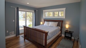 Ein Schlafzimmer mit einem Holzbett, zwei Nachttischlampen, einem Fenster und Blick ins Freie.