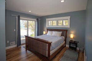 A bedroom with a wooden bed, two bedside lamps, a window, and a view of the outdoors.