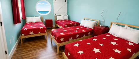 A hotel room with three beds, each with a red bedspread featuring white stars.