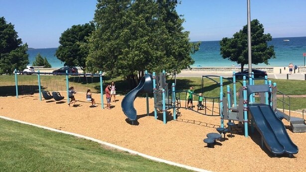 Ein Spielplatz mit Rutschen und Schaukeln in Strandnähe, mit Bäumen und blauem Himmel.