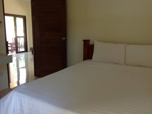 A bedroom with a large bed, a wooden door, and a view of a patio area.