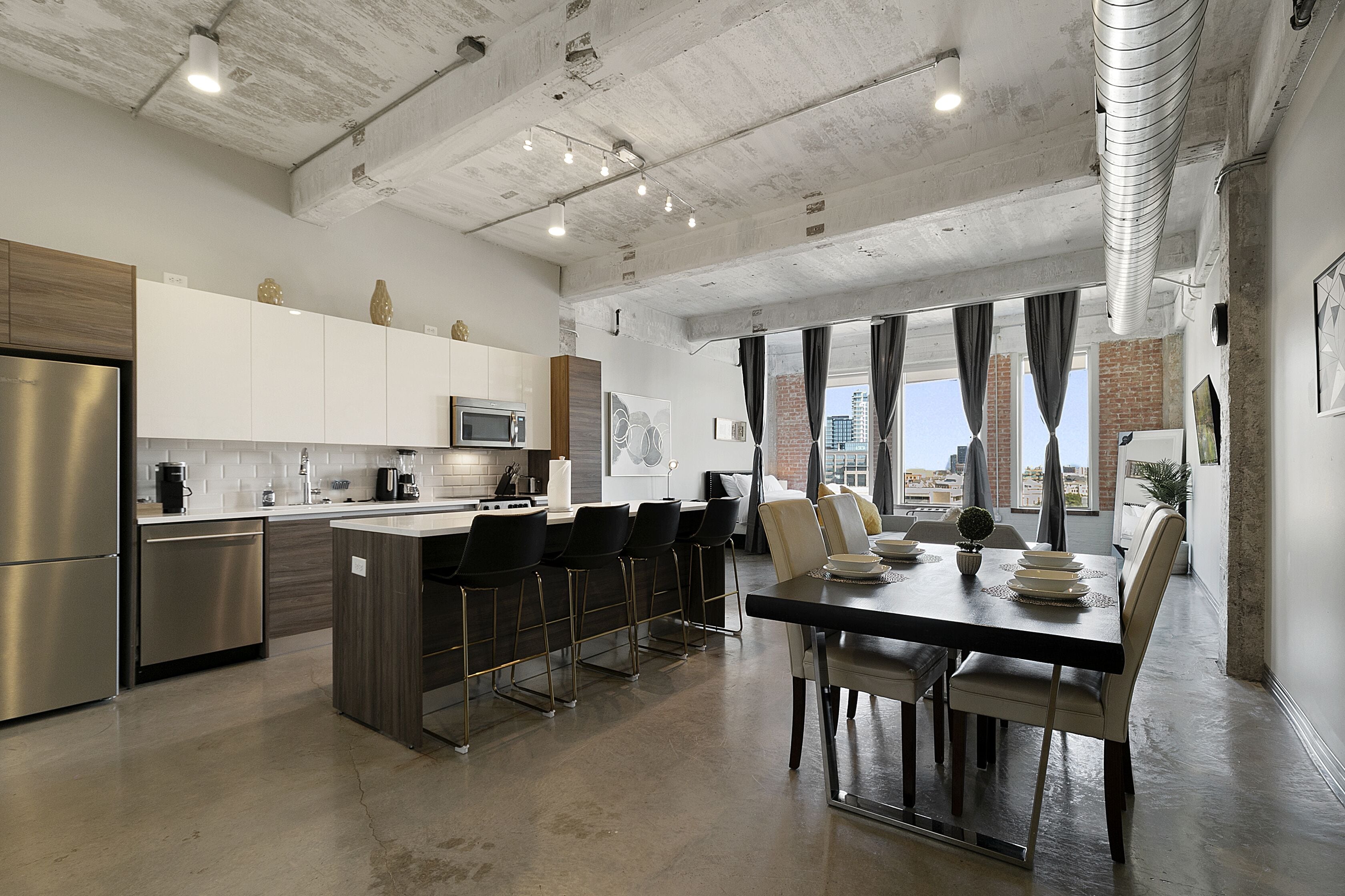 A modern kitchen with stainless steel appliances, a central island with bar stools, and a dining area with a table and chairs.