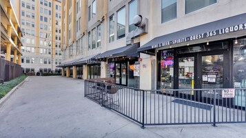 Een rij met terrasstoelen met een metalen hekwerk, een winkel met een bordje voor 'Guest Liquor' en 'Wine & Beer - Spirits - Quest 365 Liquors', en een gebouw met meerdere ramen op de achtergrond.