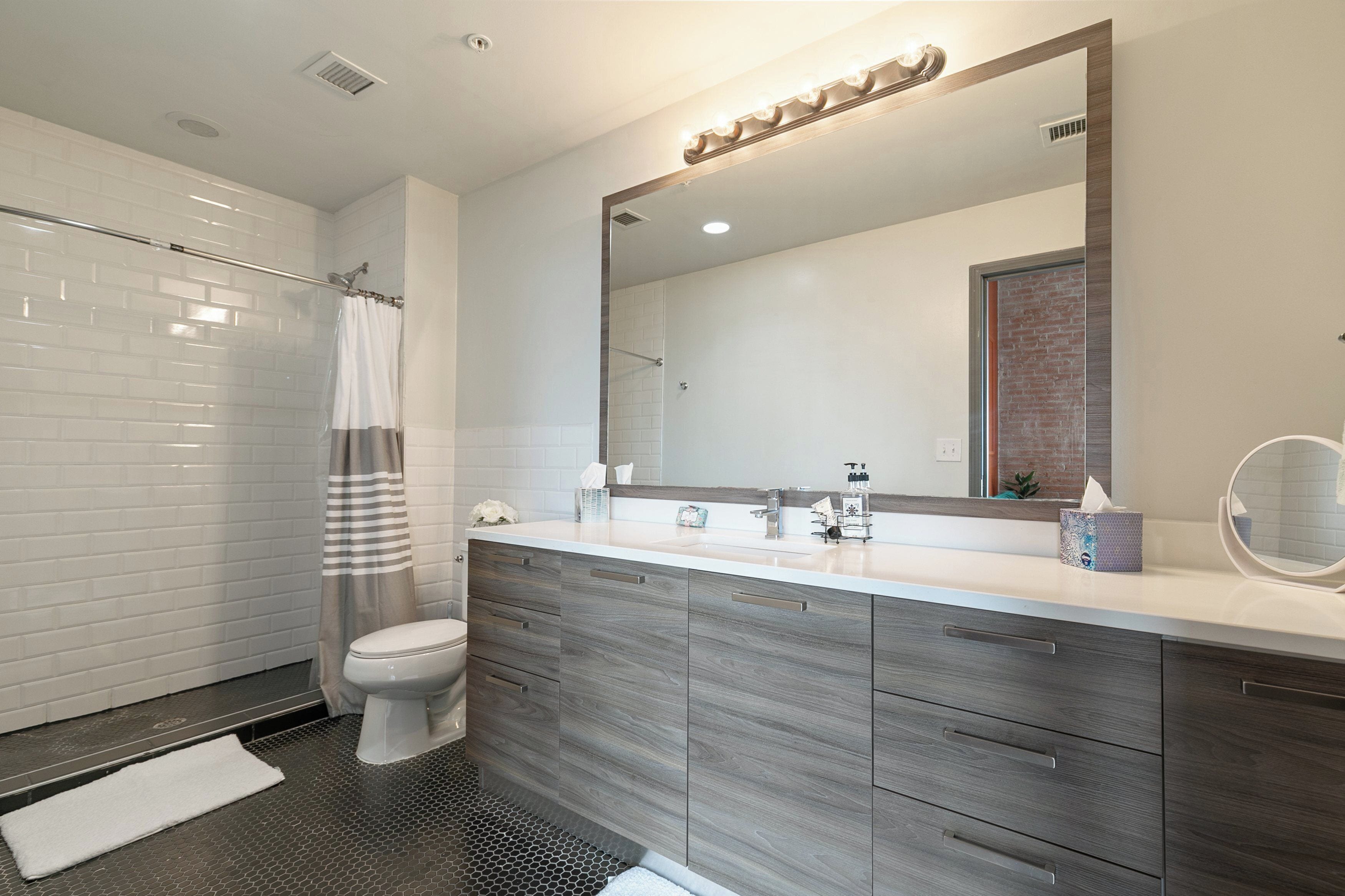 A modern bathroom with a shower, toilet, and vanity with a large mirror.