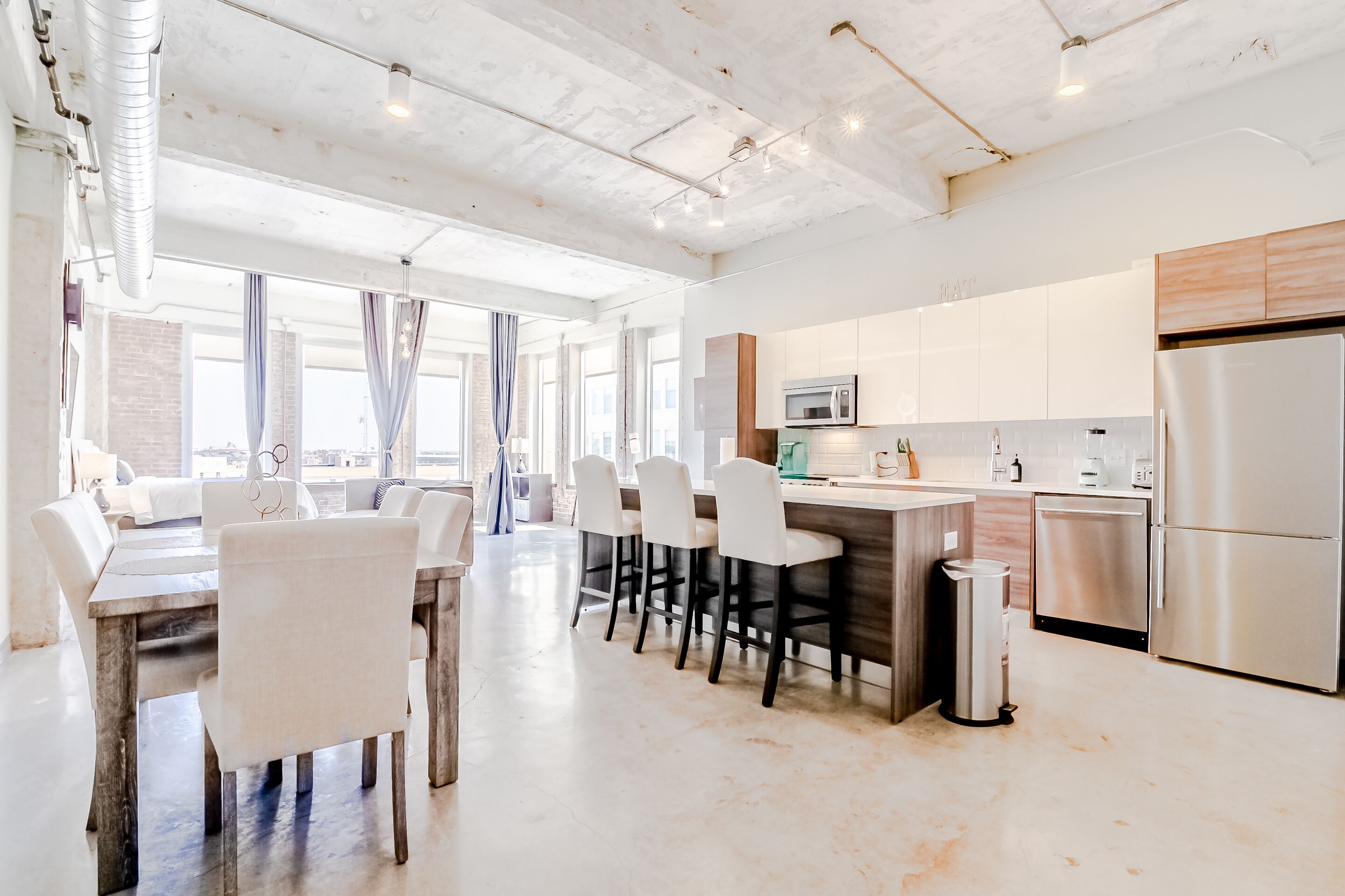 A modern kitchen with a central island, stainless steel appliances, and a dining area with white chairs.