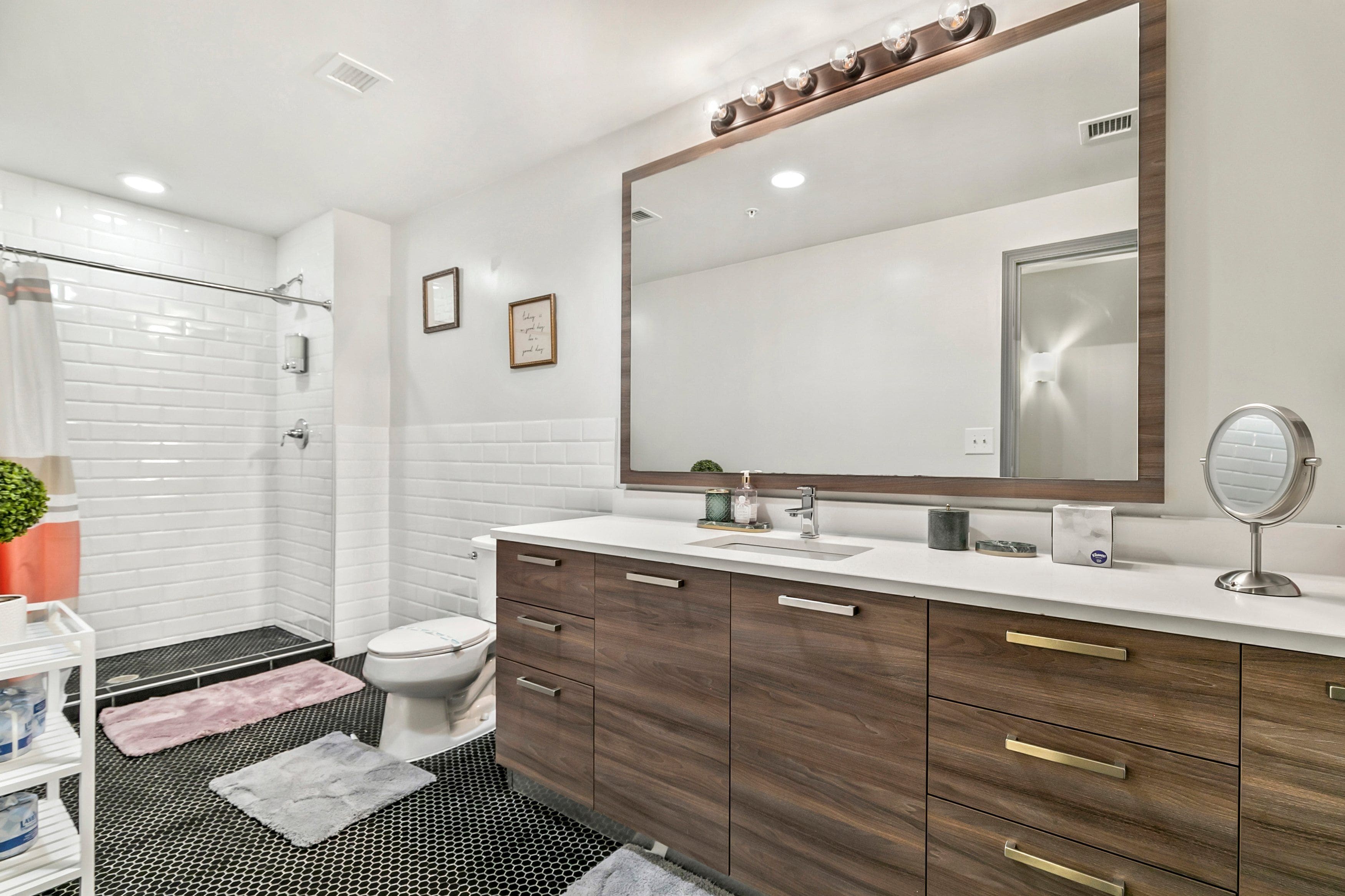 A modern bathroom with white subway tiles, a wooden vanity, a large mirror, and a shower area.