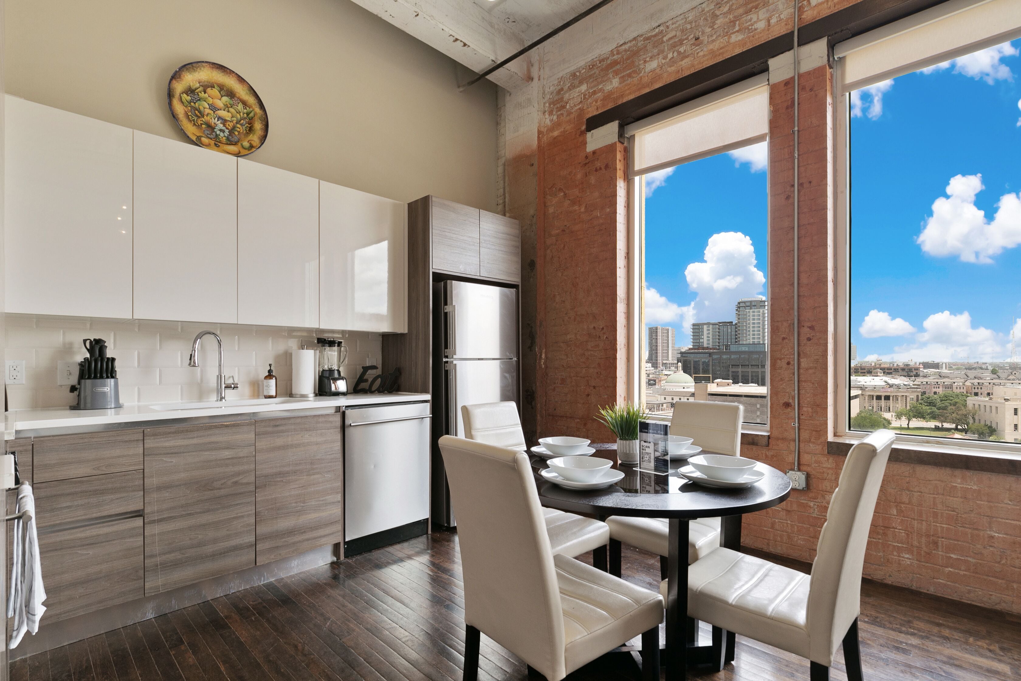 A modern kitchen with white cabinets, a stainless steel refrigerator, and a dining area with a table and chairs.