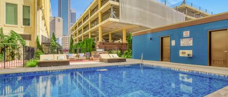 A pool area with lounge chairs and a covered seating area, surrounded by buildings and a tall skyscraper in the background.