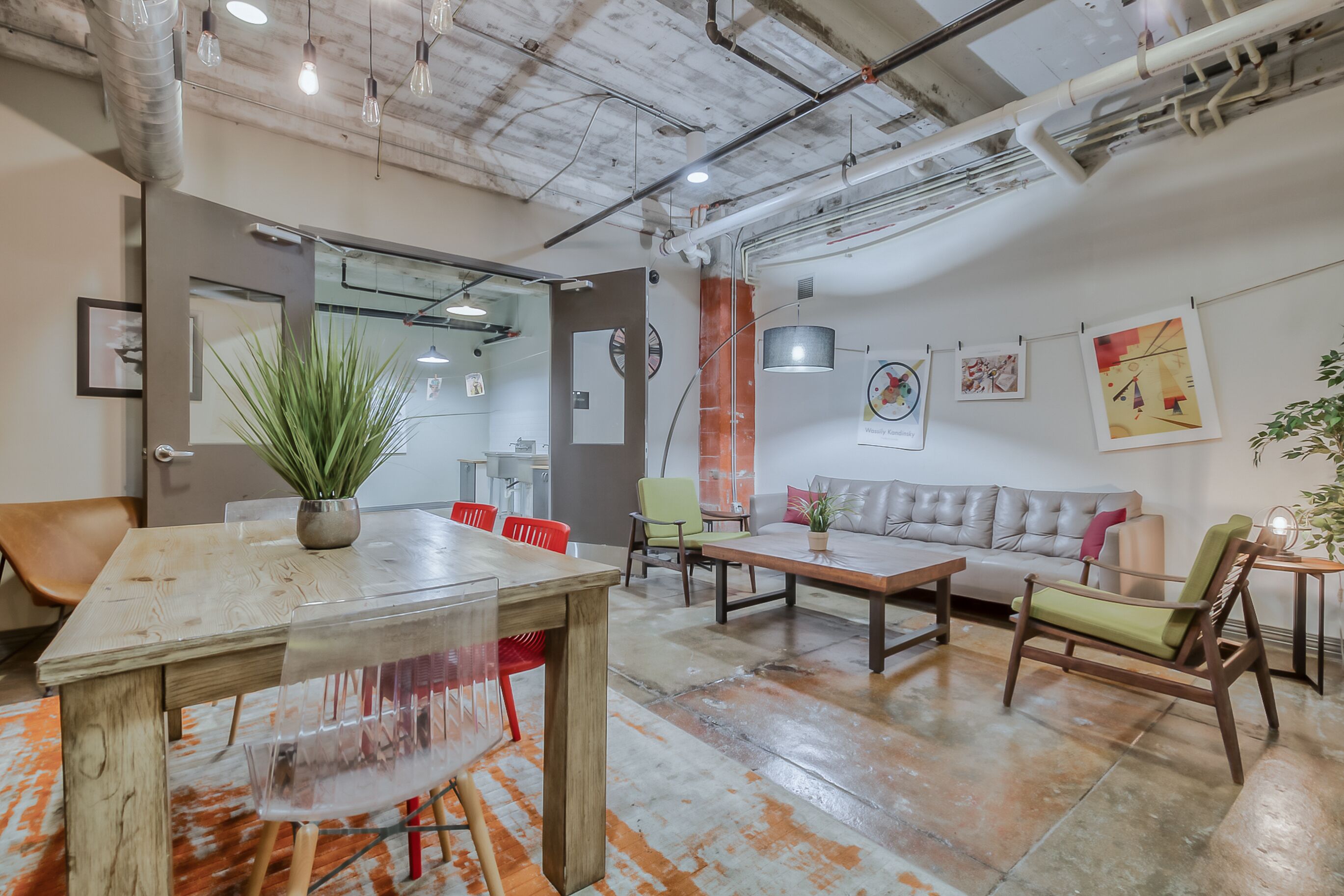 A modern office space with a wooden table, chairs, a sofa, and a potted plant.