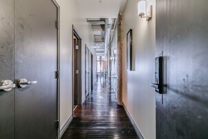Un pasillo largo y estrecho con suelo de madera oscura, puertas de metal y luminarias en las paredes.