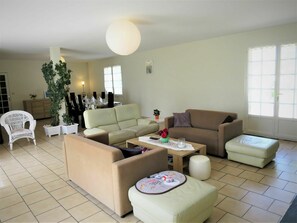 Ein Wohnzimmer mit einer Couch, Sesseln, einem Couchtisch und einem Essbereich im Hintergrund.