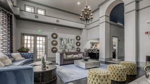 Un hall d’entrée spacieux, avec un canapé gris, des poufs ronds, un lustre et un grand tableau accroché au mur.