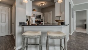 Une cuisine moderne dotée d’un îlot central, de deux tabourets de bar, d’un éclairage suspendu et d’appareils électroménagers en acier inoxydable.