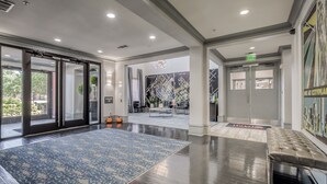Un hall d’entrée spacieux, doté d’un tapis à motifs bleus, d’un banc en cuir et d’une porte en verre donnant sur un espace détente.