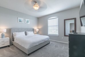 Un dormitorio con cama, mesitas de noche, cómoda, ventilador de techo y ventana con persianas.