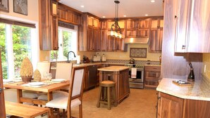 A kitchen with wooden cabinets, a dining area with a table and chairs, and an island with stools. - Luxurious Wine Country Estate with Mountain and Pastoral Views (Wilsonville)