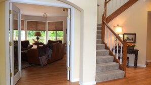A home interior with a wooden staircase, a living room with a sofa and a coffee table, and a view through a glass door. - Luxurious Wine Country Estate with Mountain and Pastoral Views (Wilsonville)