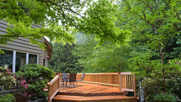 A wooden deck with a staircase leading to a covered patio area, surrounded by lush greenery and a house. - Luxurious Wine Country Estate with Mountain and Pastoral Views (Wilsonville)