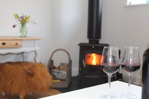 Ein gemütliches Zimmer mit Kamin, einem fellüberzogenen Sessel und zwei Gläsern Rotwein auf einem Tisch.