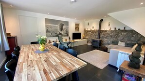 Ein modernes Wohnzimmer mit einem Holzespeisetisch, blauen Stühlen, einem Steinkamin und einem Fernseher.