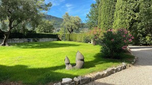 Ein gepflegter Rasen mit einer Steinskulptur, einem Kiesweg und einer Hecke.