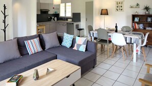 Una sala de estar moderna con un sofá gris, una mesa de centro de madera y un comedor con una mesa dispuesta para cuatro personas.