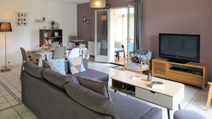 Una sala de estar moderna con un sofá gris, un televisor sobre un mueble de madera y una zona de comedor con una mesa y sillas.