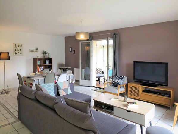 A modern living room with a grey sofa, a TV on a wooden stand, and a dining area with a table and chairs.