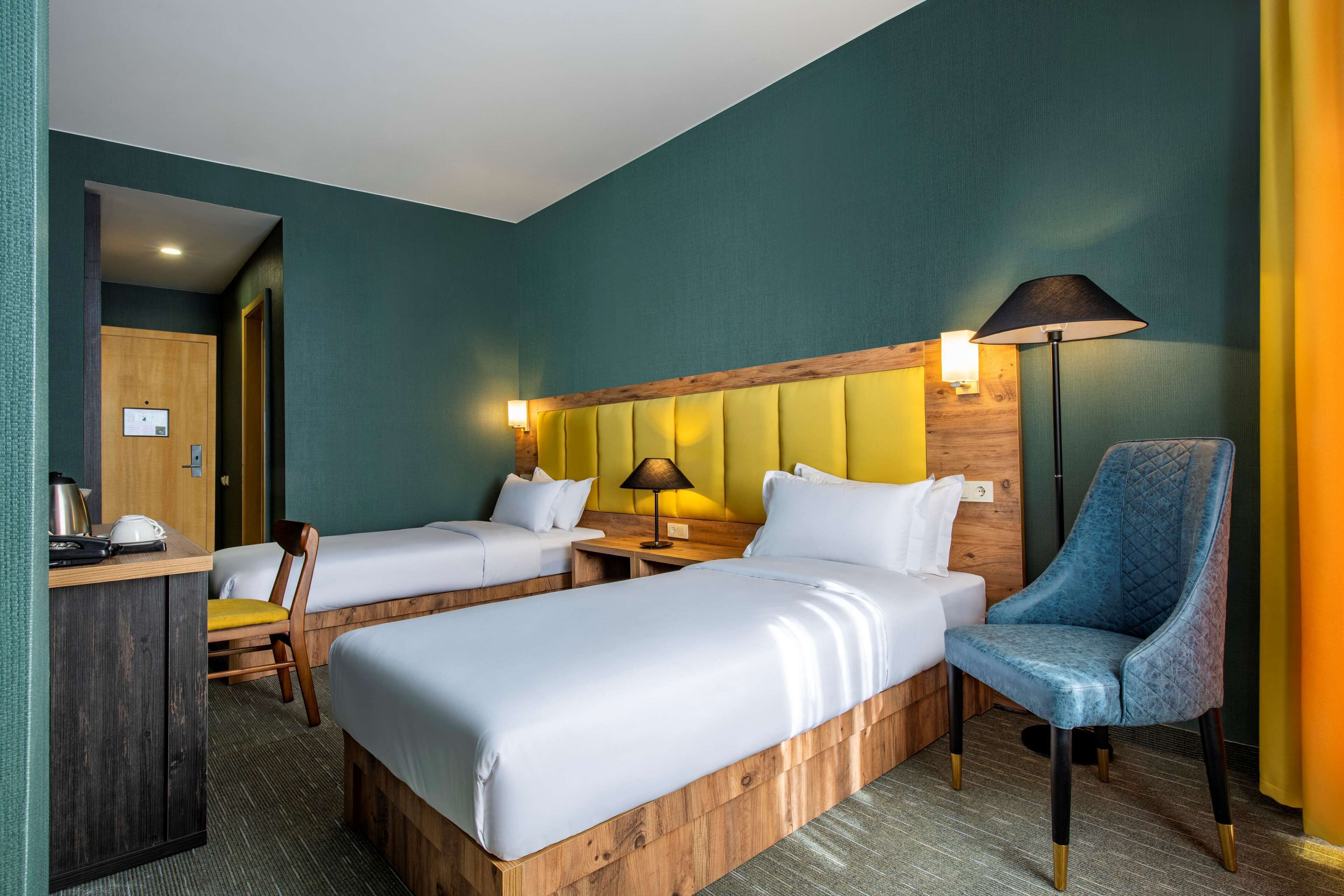Una habitación de hotel con dos camas, un escritorio con lámpara y una silla.