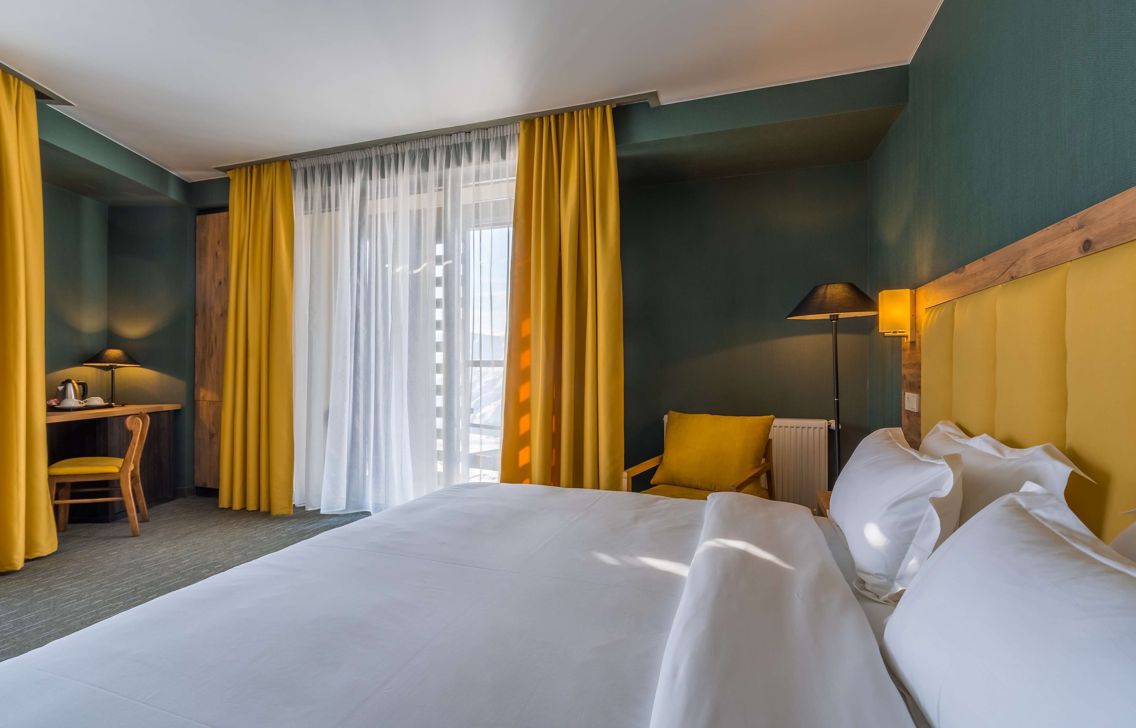 A hotel room with a large bed, a desk with a chair, and a lamp.