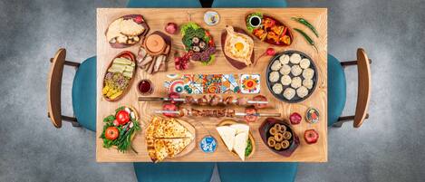 A wooden table with various foods and drinks, surrounded by blue chairs.