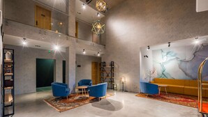 Un vestíbulo moderno con techo alto, luminarias geométricas, un gran mural abstracto y zonas de estar en azul.