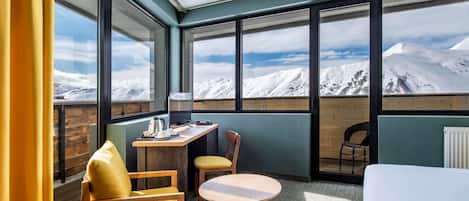 Ett hotellrum med ett stort fönster med utsikt över bergen, ett skrivbord i trä med en stol och en säng.