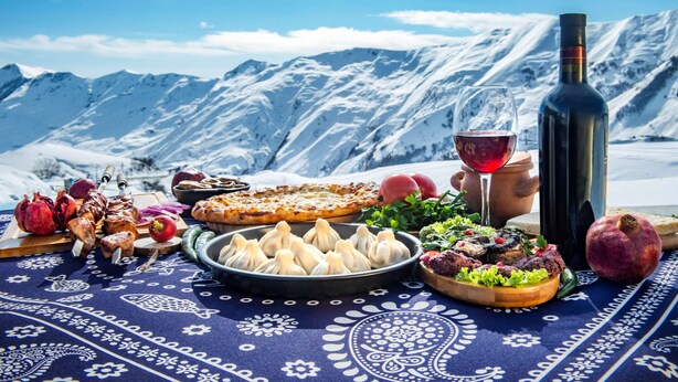 Una mesa con comida y una botella de vino frente a un paisaje montañoso nevado.