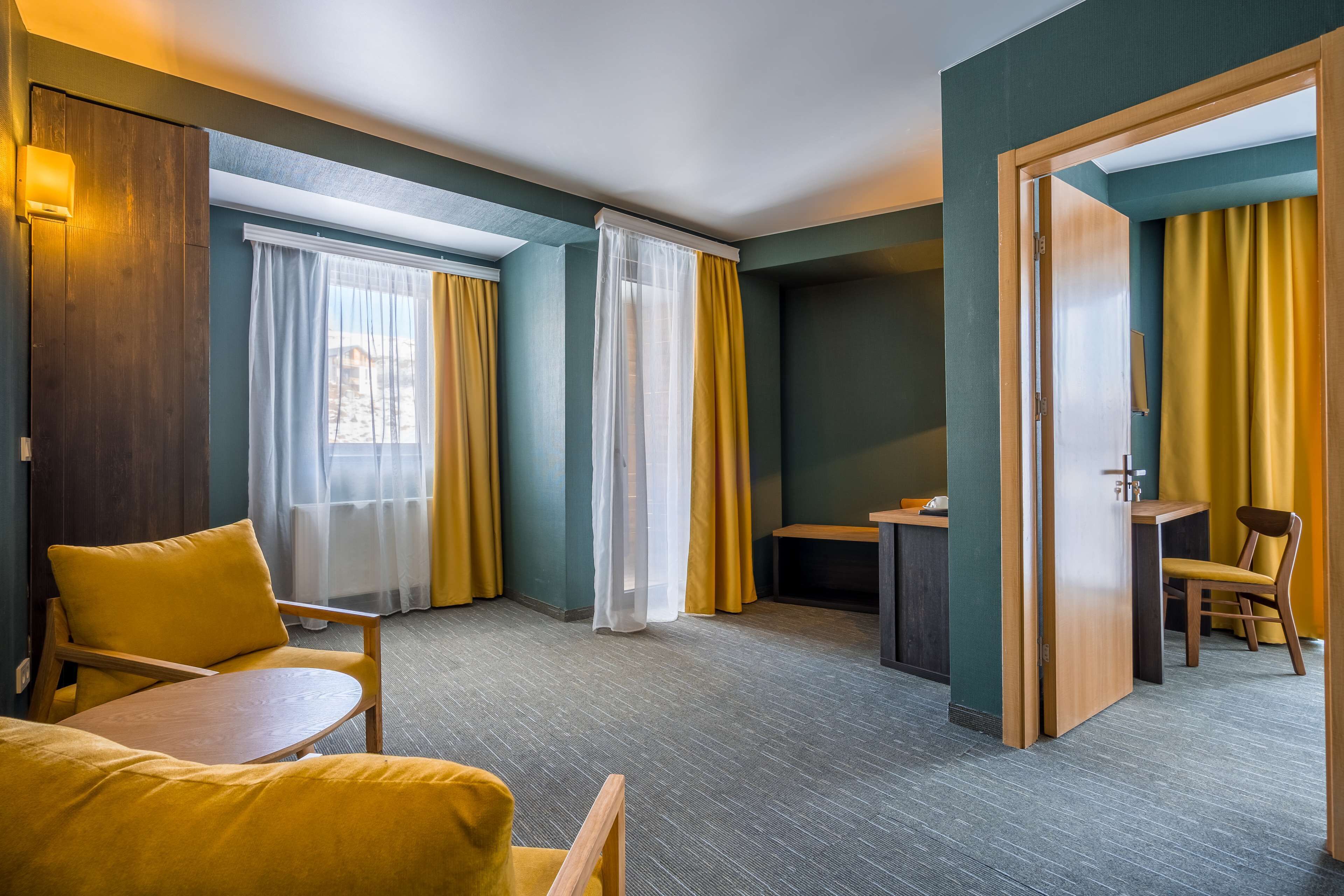 A hotel room with a wooden chair, a small table, and a desk with a chair.