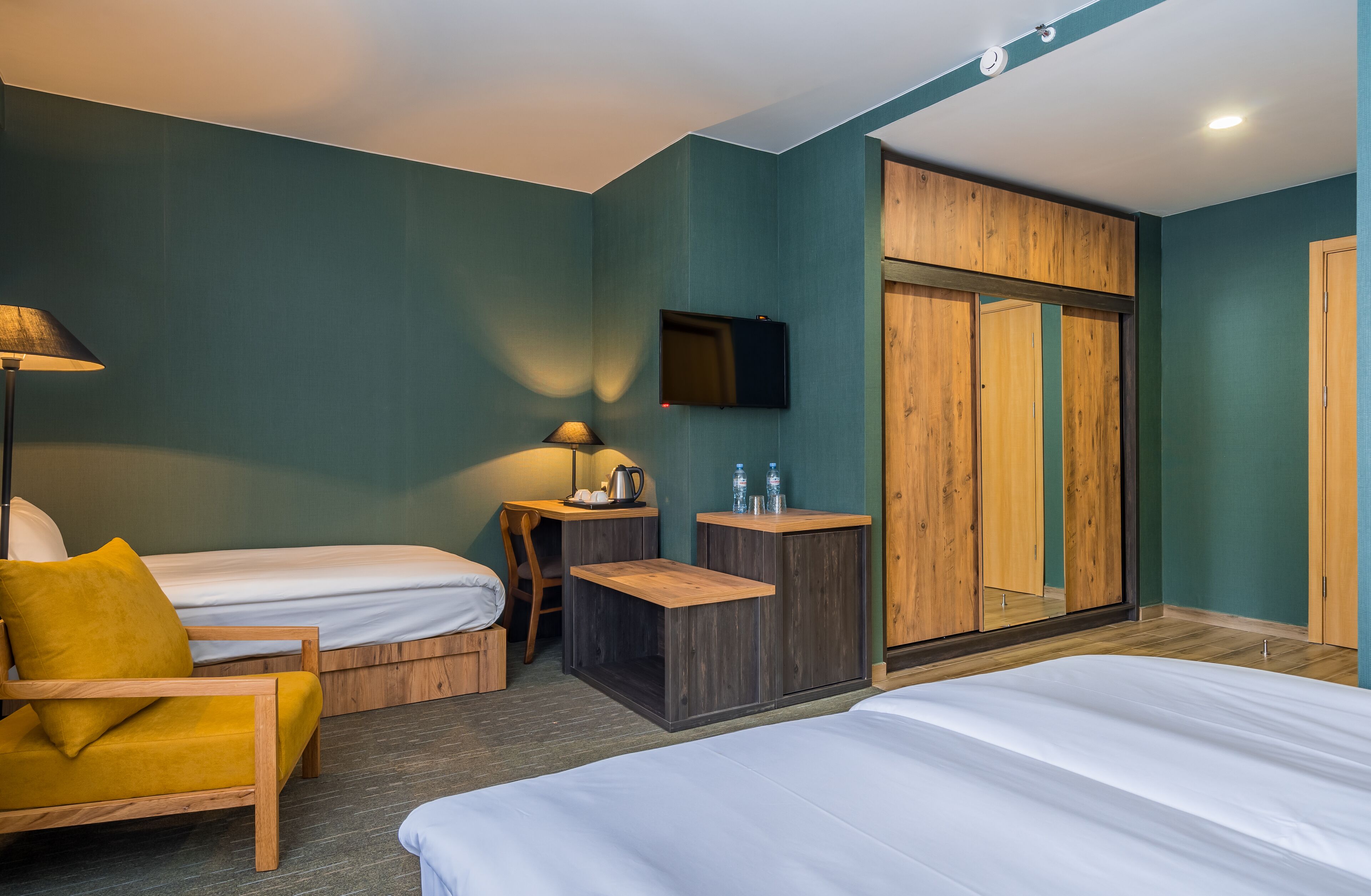 A hotel room with two beds, a wooden wardrobe, a TV, and a small table with a lamp.
