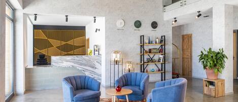 Un interior moderno con pared de mármol, sillones azules, una mesa redonda y una planta grande.