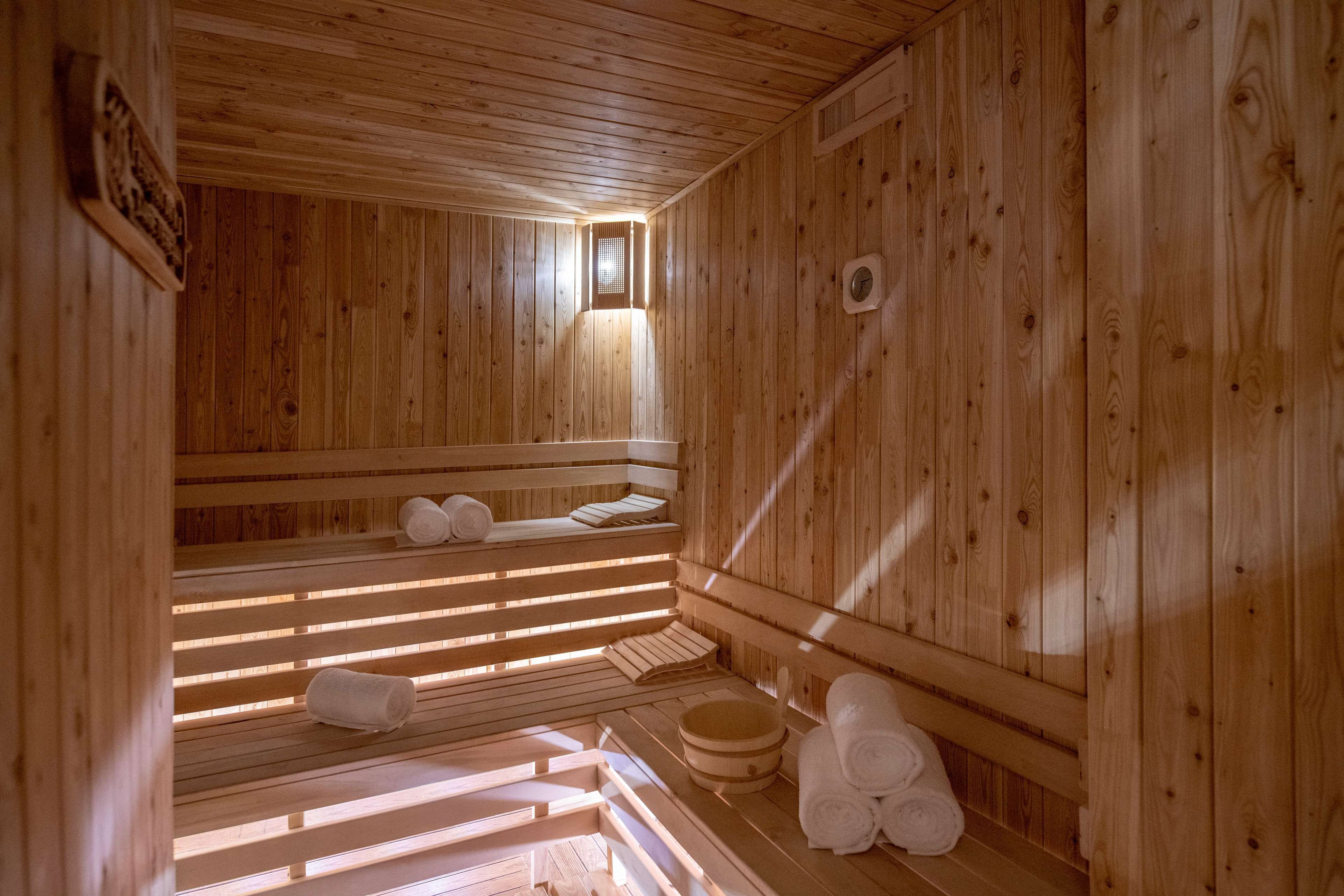 A wooden sauna with benches and benches, towels, and a wooden bucket.
