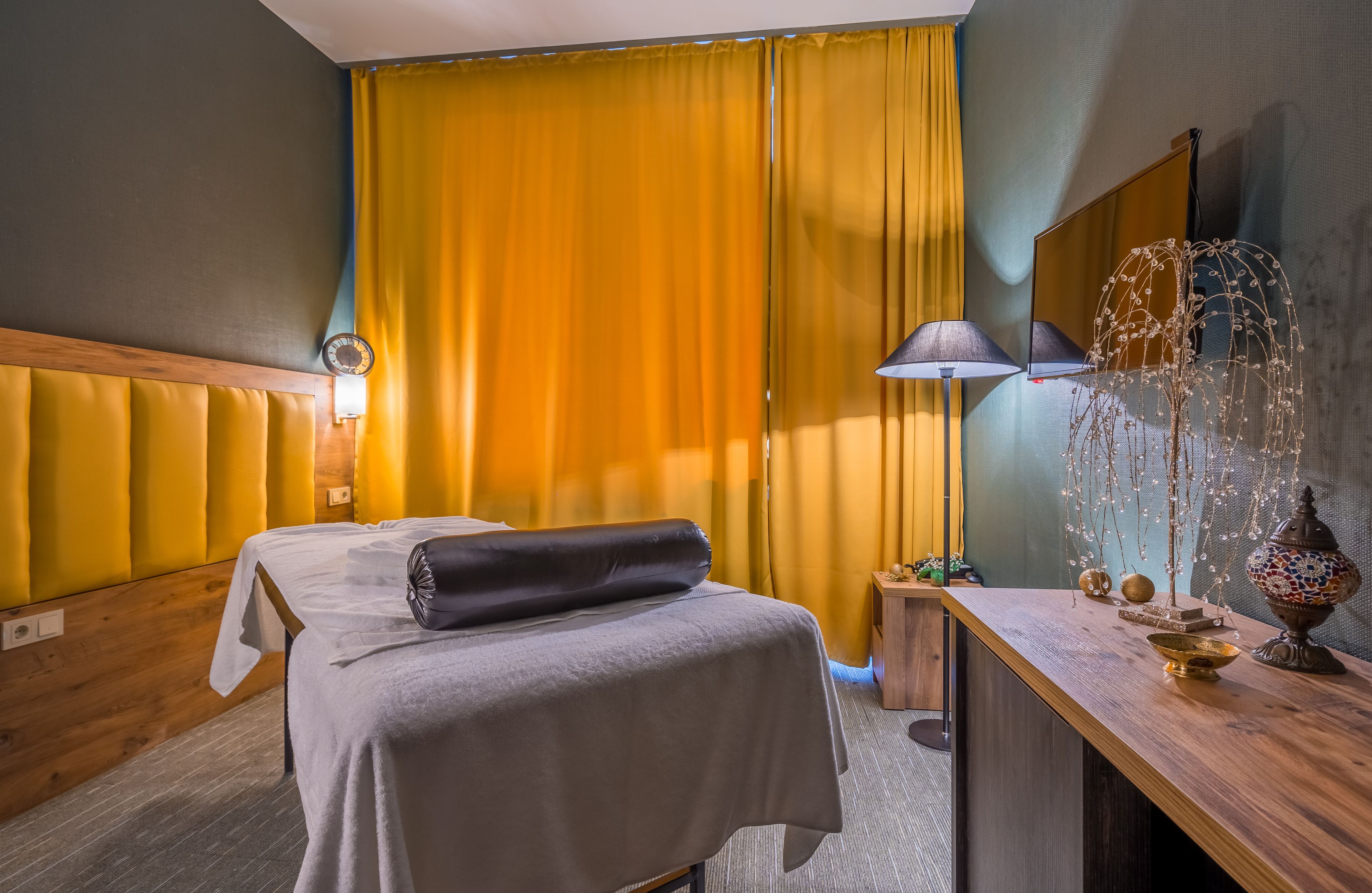 A hotel room with a bed, a wooden headboard, a nightstand with a lamp, and a decorative mirror.