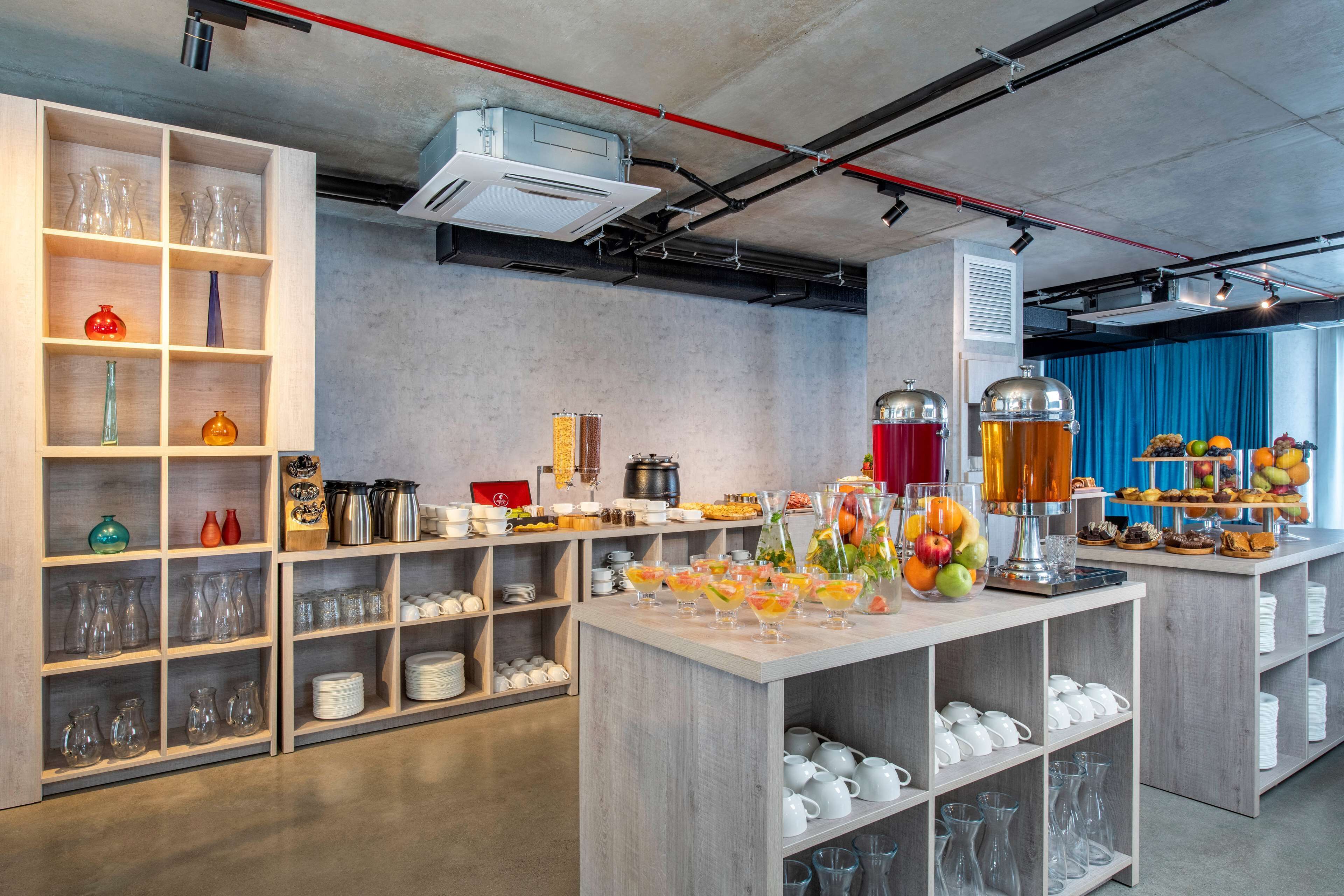 A modern kitchen with open shelving displaying glassware and kitchenware, a central island with fruit and beverages, and a blue curtain in the background.