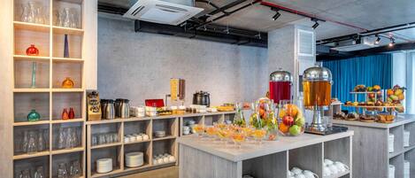 A modern kitchen with open shelving displaying glassware and kitchenware, a central island with fruit and beverages, and a blue curtain in the background.