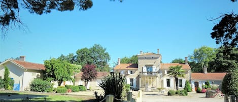 A traditional building with a central entrance, surrounded by a well-maintained garden and trees.